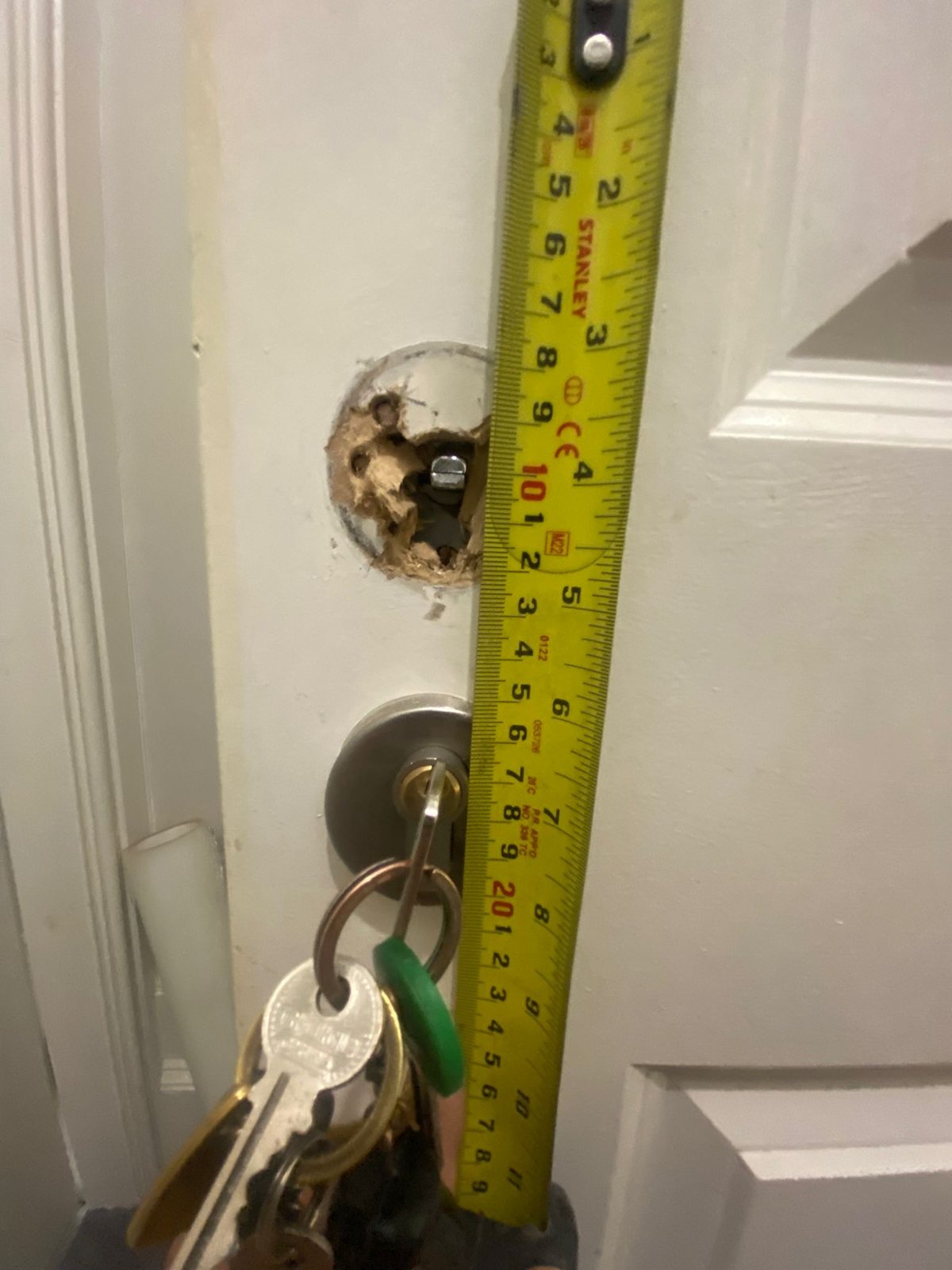 Tape measure held against a door where the old lock has been removed, keys in the cylinder below
