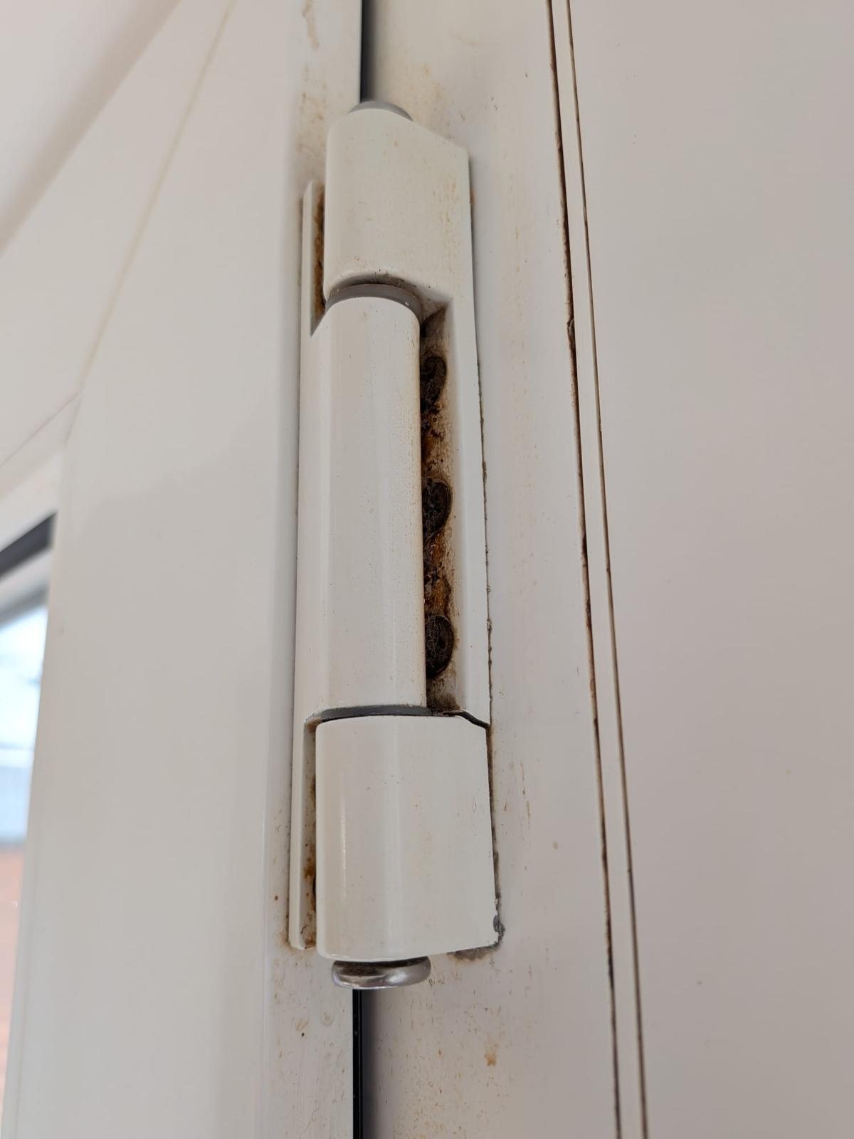 Worn uPVC door flag hinge with corroded fixing screws behind it