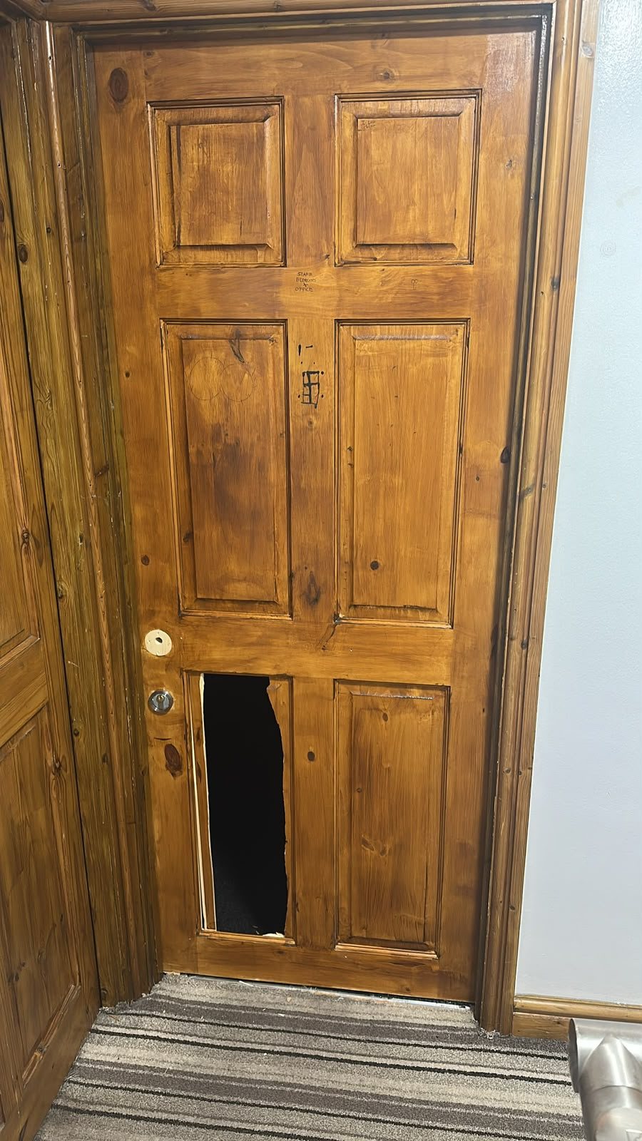 Timber panelled door with its lower panel kicked through, leaving a ragged hole