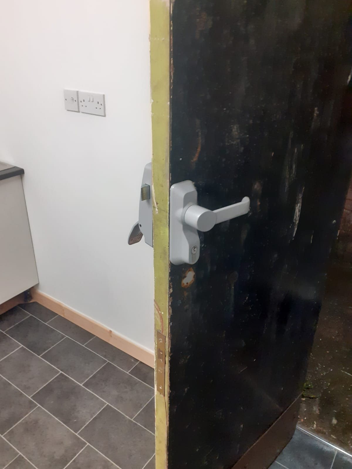New grey lever handle and rim lock fitted to a black timber door
