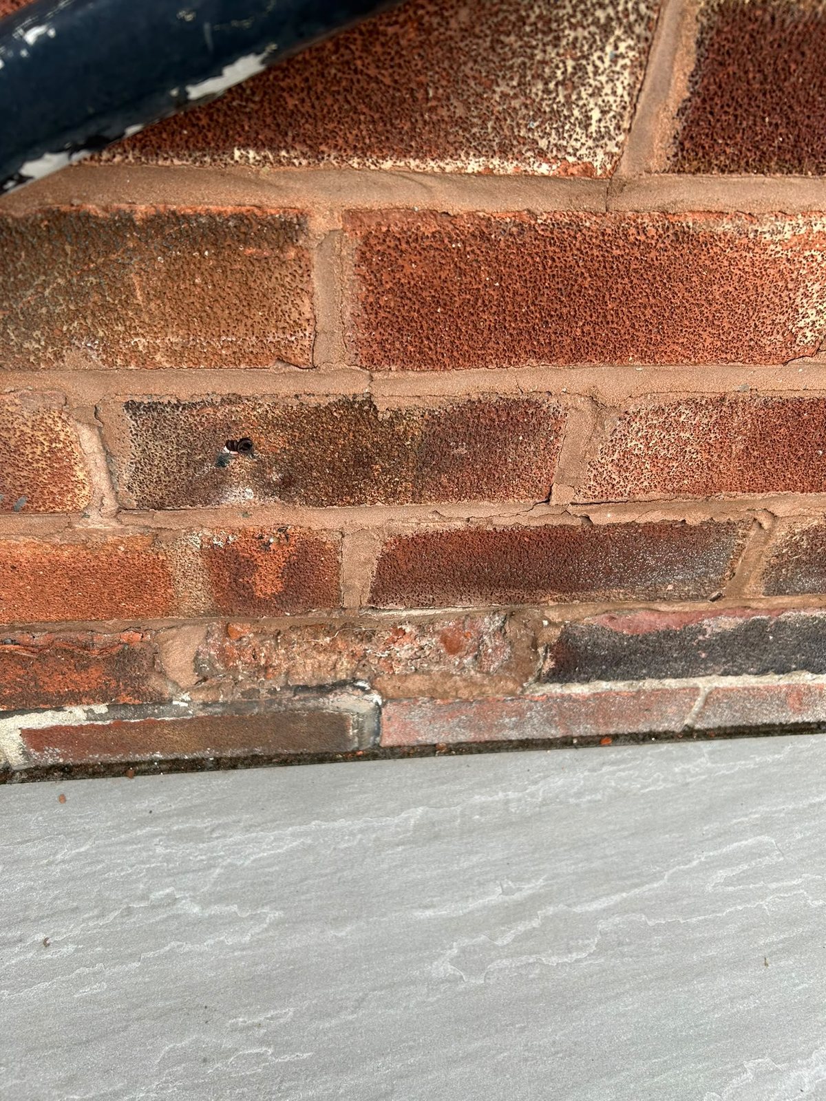 Spalled bricks in the bottom courses Close view of the bottom courses of a brick wall above grey paving, with spalled and crumbling brick faces