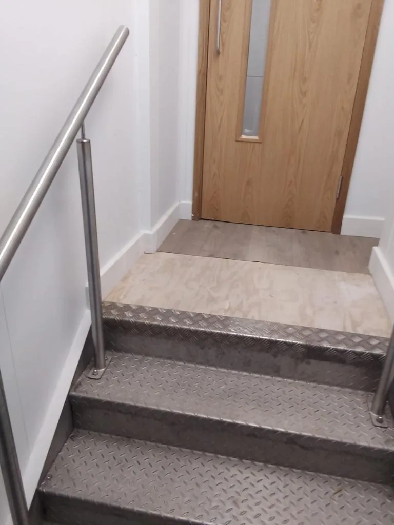 Oak-veneered fire door with a vision panel at the top of a short flight of steel stairs