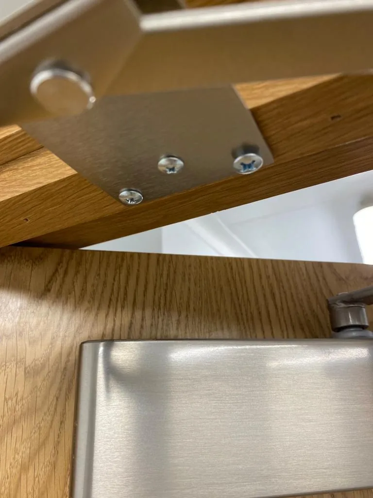 Close-up of an overhead door closer arm and its fixing bracket at the head of an oak-veneered fire door