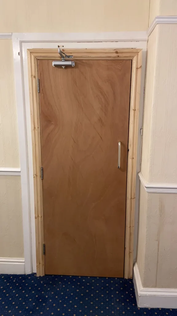 Plywood-faced fire door with an overhead closer and pull handle in a new softwood frame
