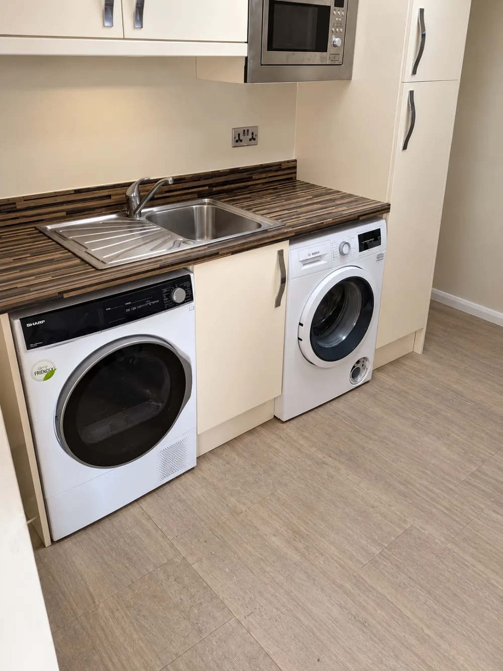 Finished utility area in a converted garage with sink, worktop, washing machine, tumble dryer and re-installed kitchen units