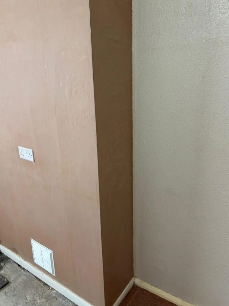 Fireplace closed off and skimmed, with a vent grille fitted Former fireplace boarded and freshly skimmed, with a white vent grille near the new skirting board