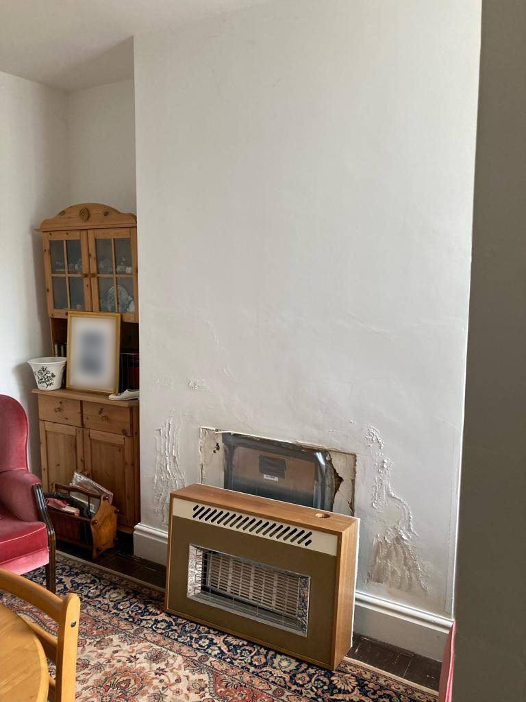 Old gas fire on a chimney breast Old gas fire in a wood-effect case against a white chimney breast, with broken plaster round the opening behind it