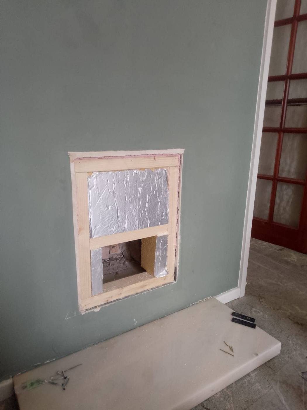 Stud frame and insulation in a fireplace opening Timber stud frame built inside a fireplace opening in a green wall, with insulation fitted between the studs