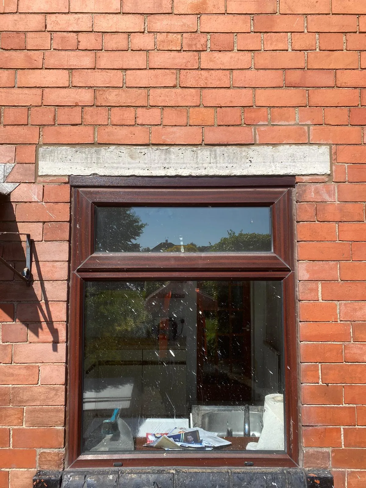 Concrete lintel above a brown-framed window in a red brick wall