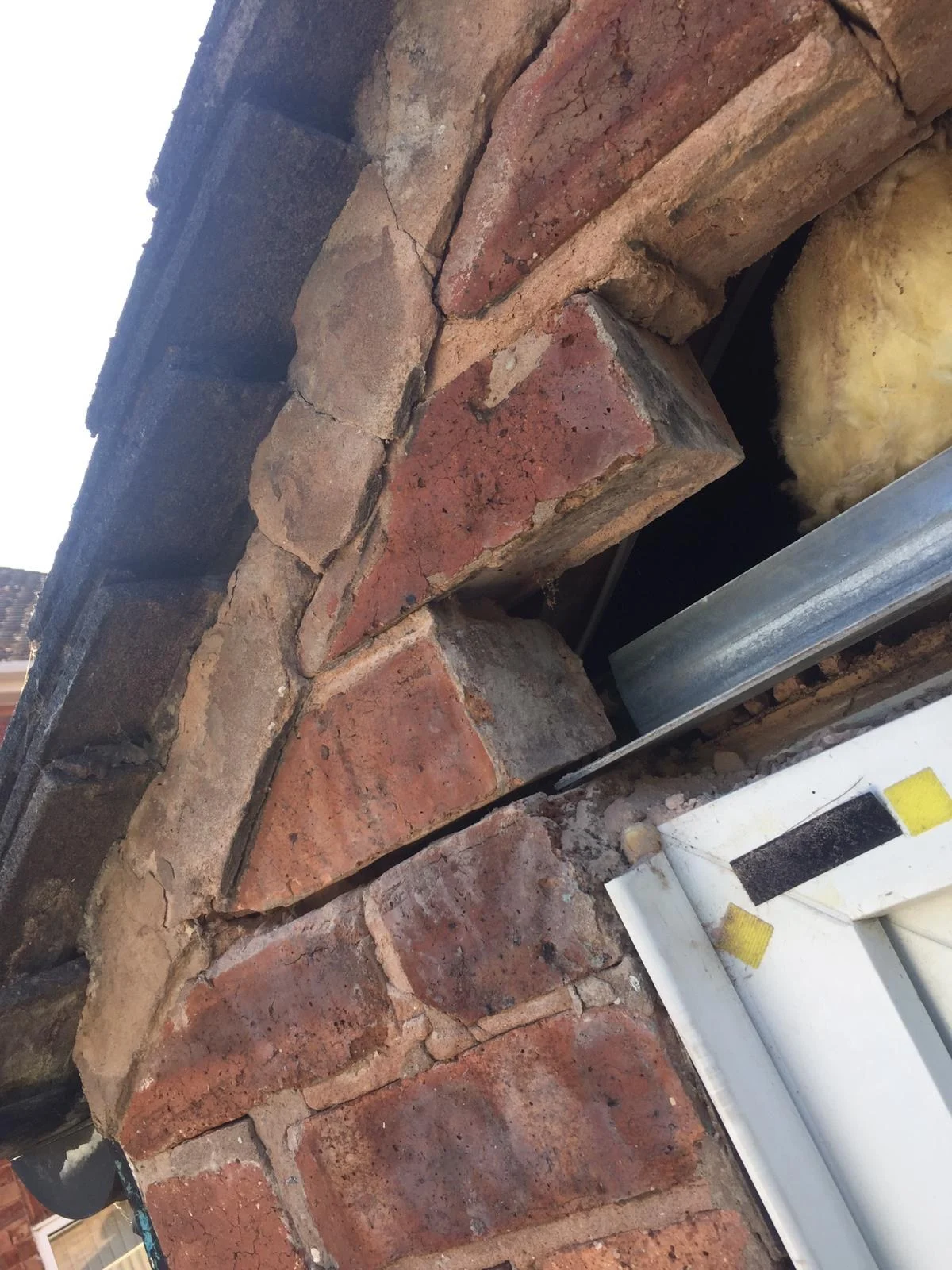 Brickwork opened up above a door frame, with a galvanised steel lintel in the opening and insulation visible behind