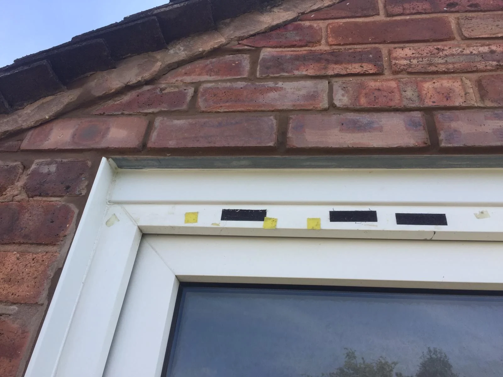 Close view of the edge of a steel lintel above a white door frame, with repointed brickwork over it