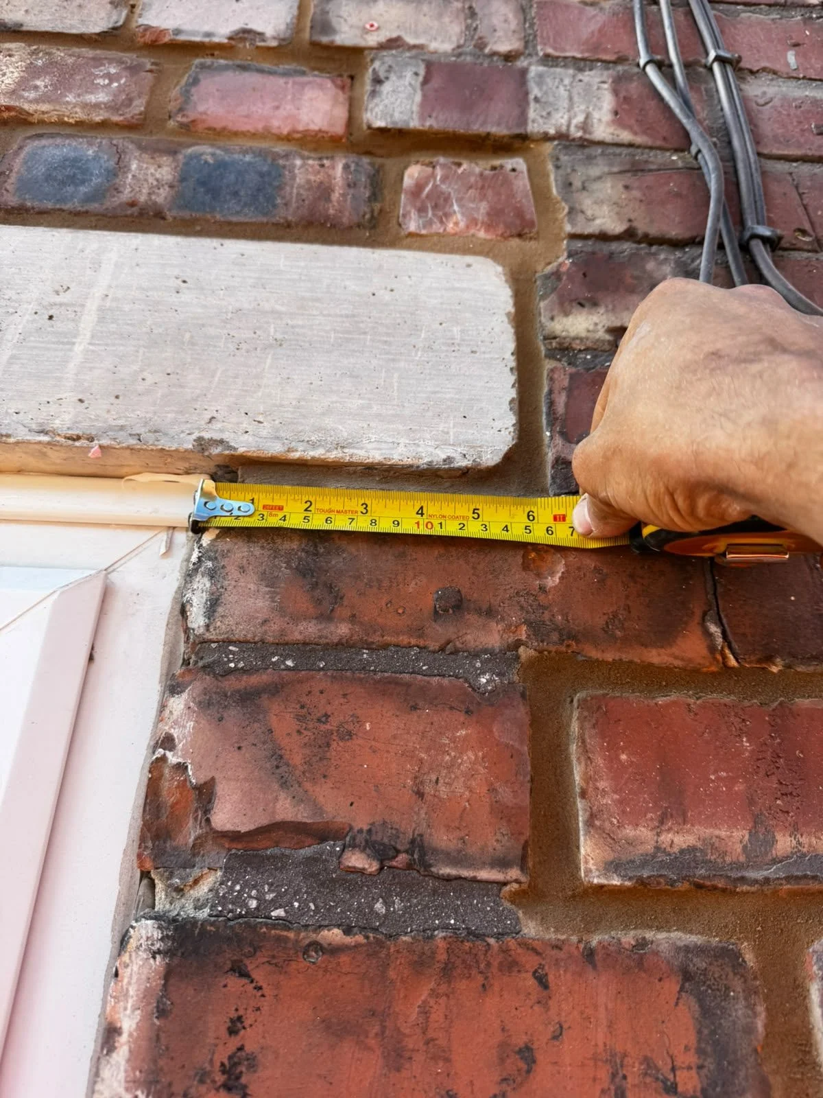 Tape measure checking the end bearing of a new concrete lintel where it sits on the brickwork beside a window opening