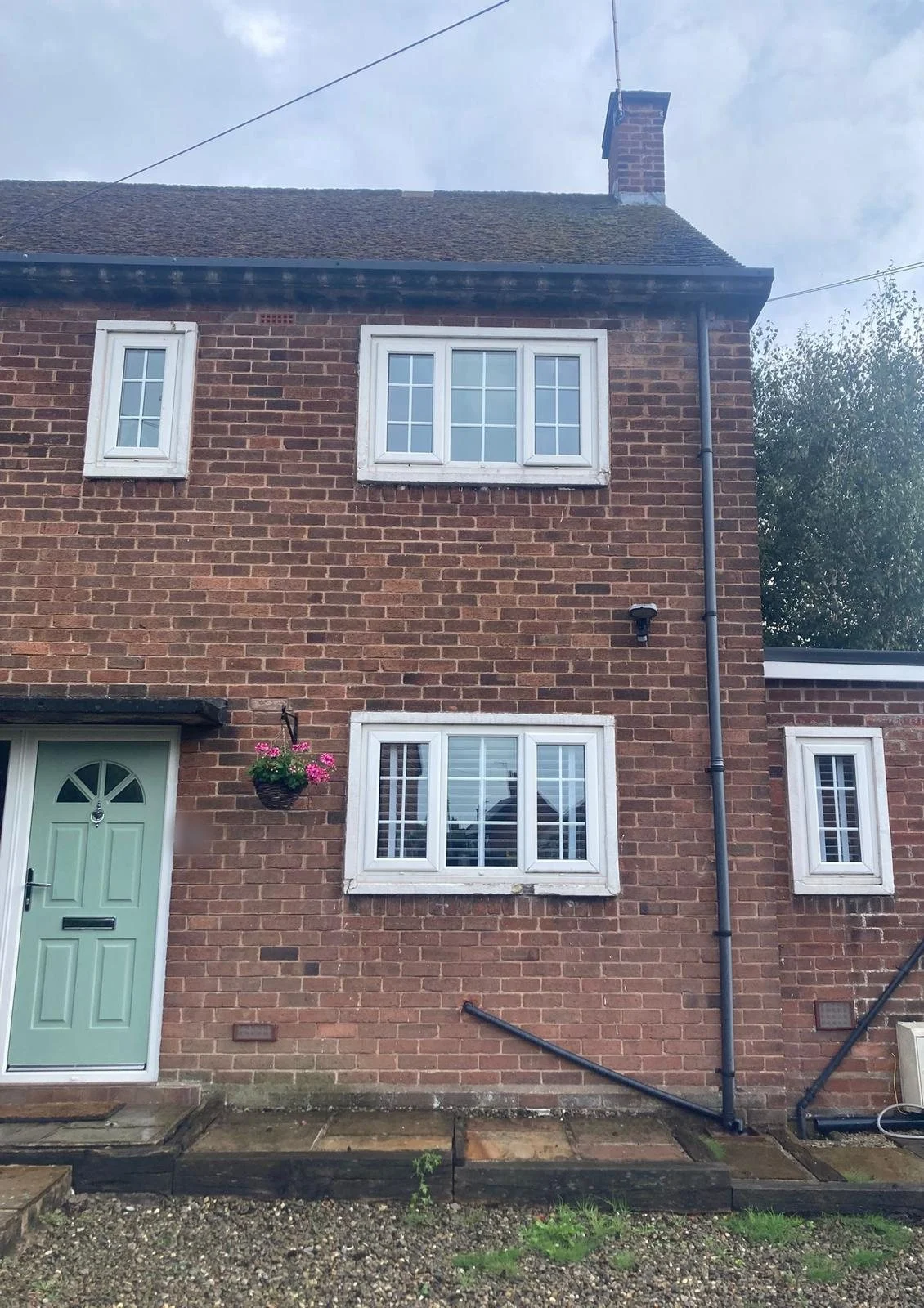 Front of a two-storey red brick house with white painted concrete surrounds framing each window