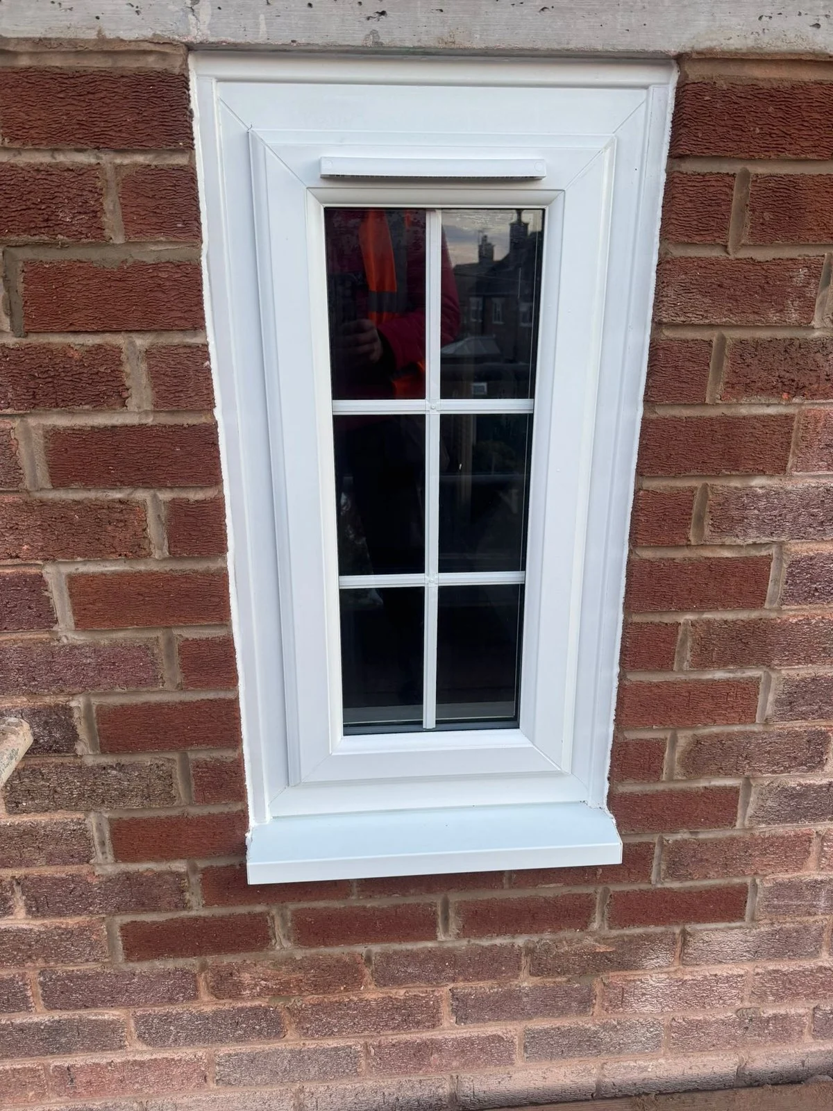 Narrow white uPVC window with a trickle vent, a concrete lintel above and new brickwork either side