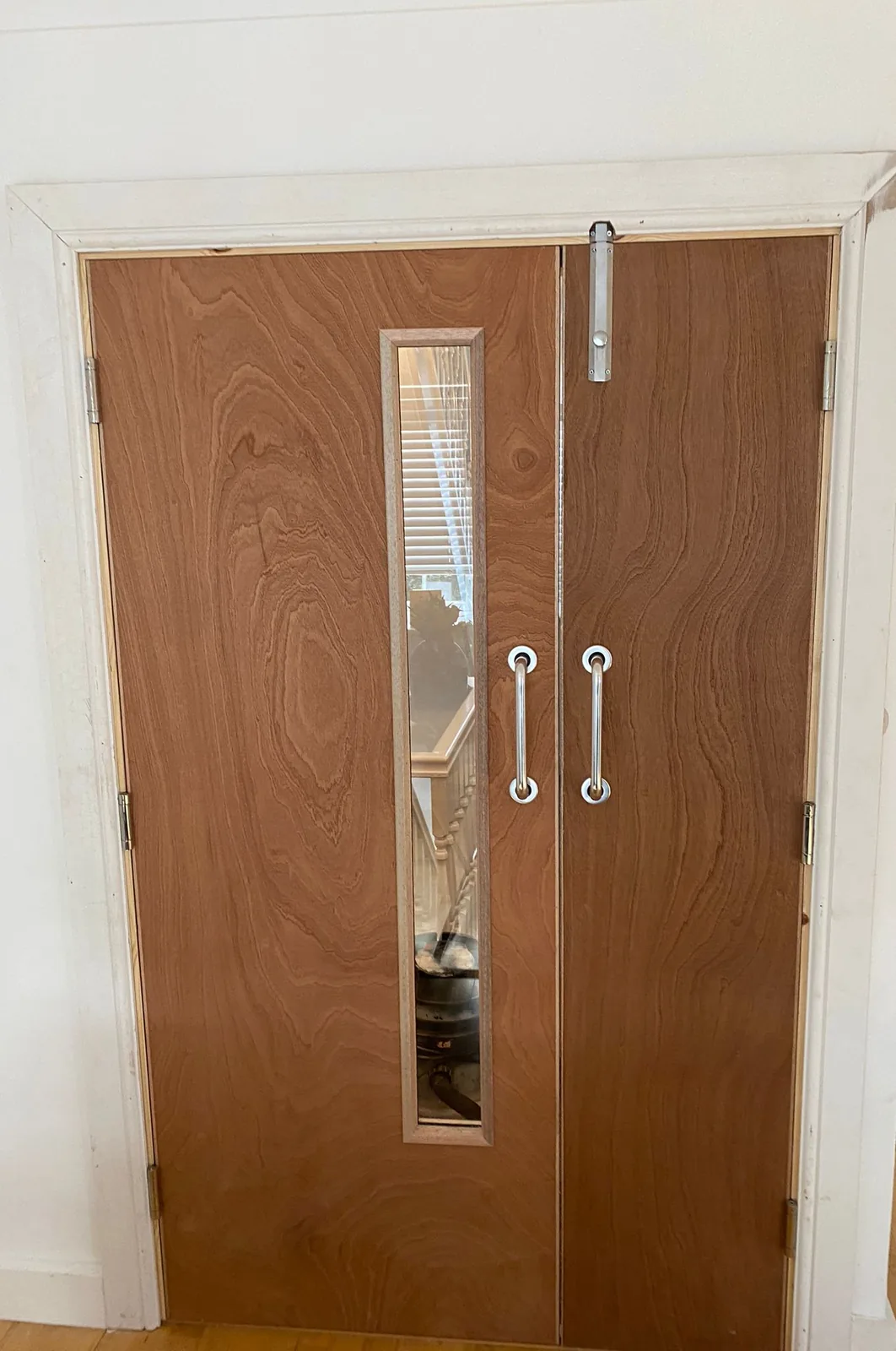 The other face of a pair of plywood-faced fire doors, with two pull handles and a narrow vision panel