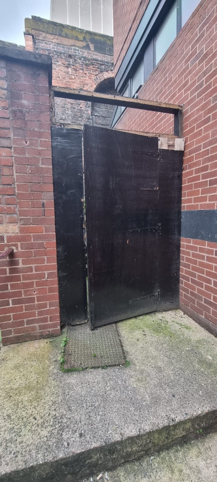 Dark timber yard door sitting out of square in a brick opening
