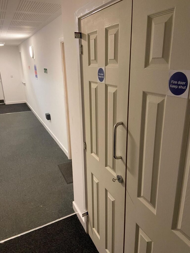 Pair of plywood-faced fire doors with vision panels in the corridor of a block of flats